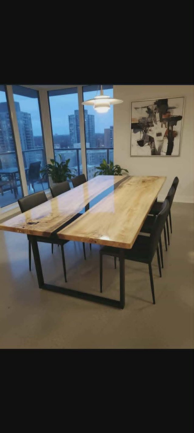 Grande table de salle à manger en bois massif à bordure naturelle avec rivière d'époxy transparente et pieds en métal noir, devant de grandes fenêtres donnant sur la ville — Les Bois Rustiques MG