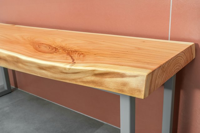 Banc en bois massif à bordure naturelle sur pieds métalliques fins, dans une salle de bain aux tuiles terracotta — idée de projet